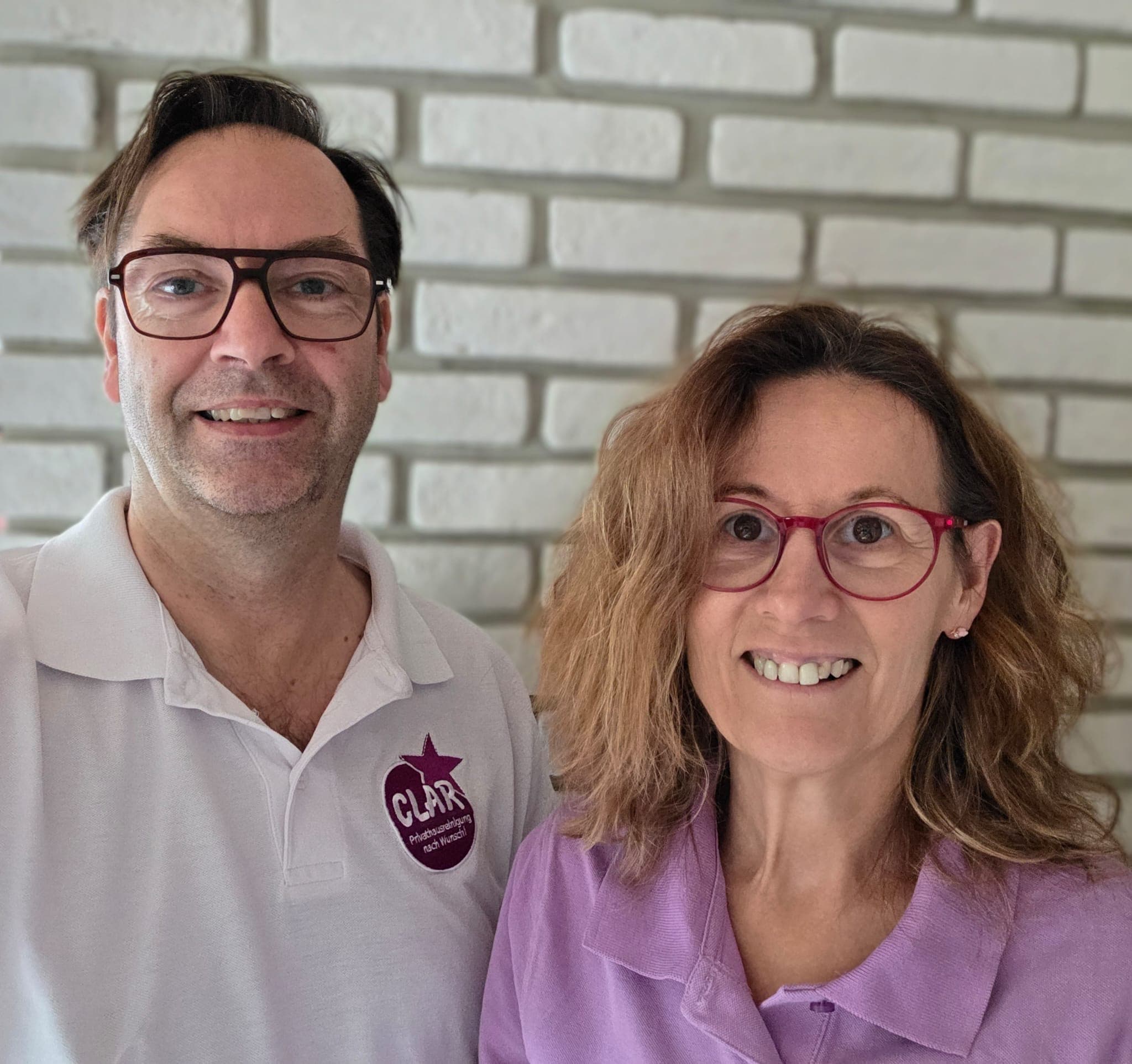 Lars Jäschke und Claudia Kämmerer in CLAR-Poloshirts vor einer hellen Backsteinwand